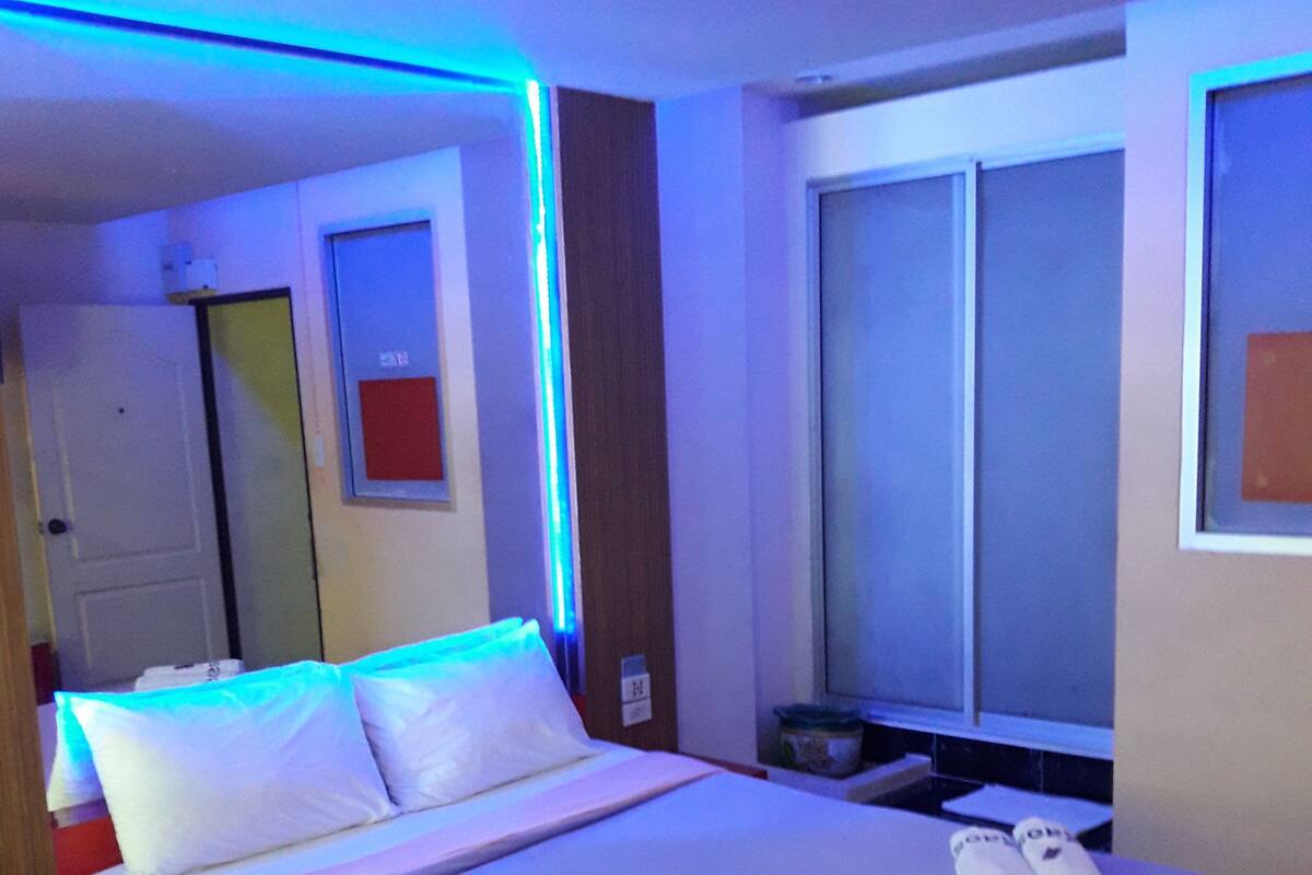 Una habitación de hotel con cama, ventana, puerta y mesita de noche.