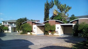 A row of single-story houses with curved roofs, surrounded by greenery and a clear sky.