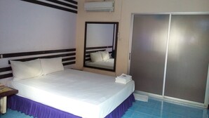 A hotel room with a bed, a mirror, a wardrobe, and an air conditioning unit.