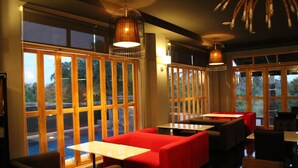 A restaurant with large windows, red seating, and hanging pendant lights.