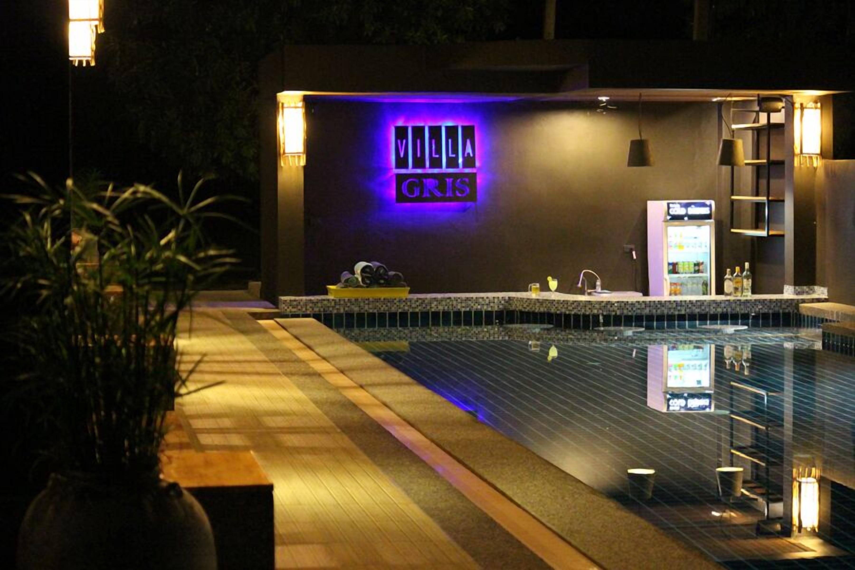 A pool area with a sign reading "Villa Gris" and a bar area with a refrigerator and shelves.