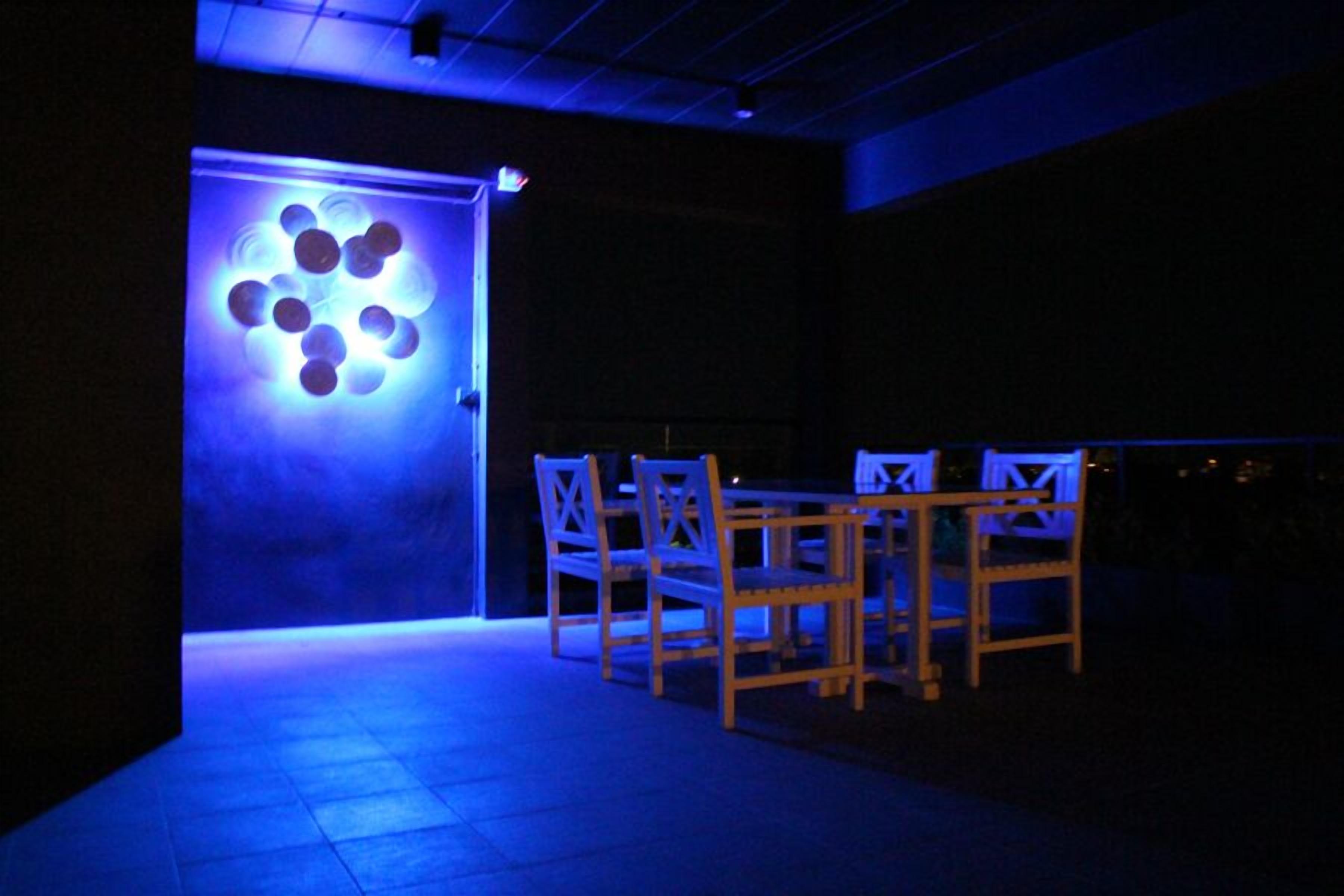 A dimly lit room with a table and chairs, a blue light feature on the wall, and a door leading outside.