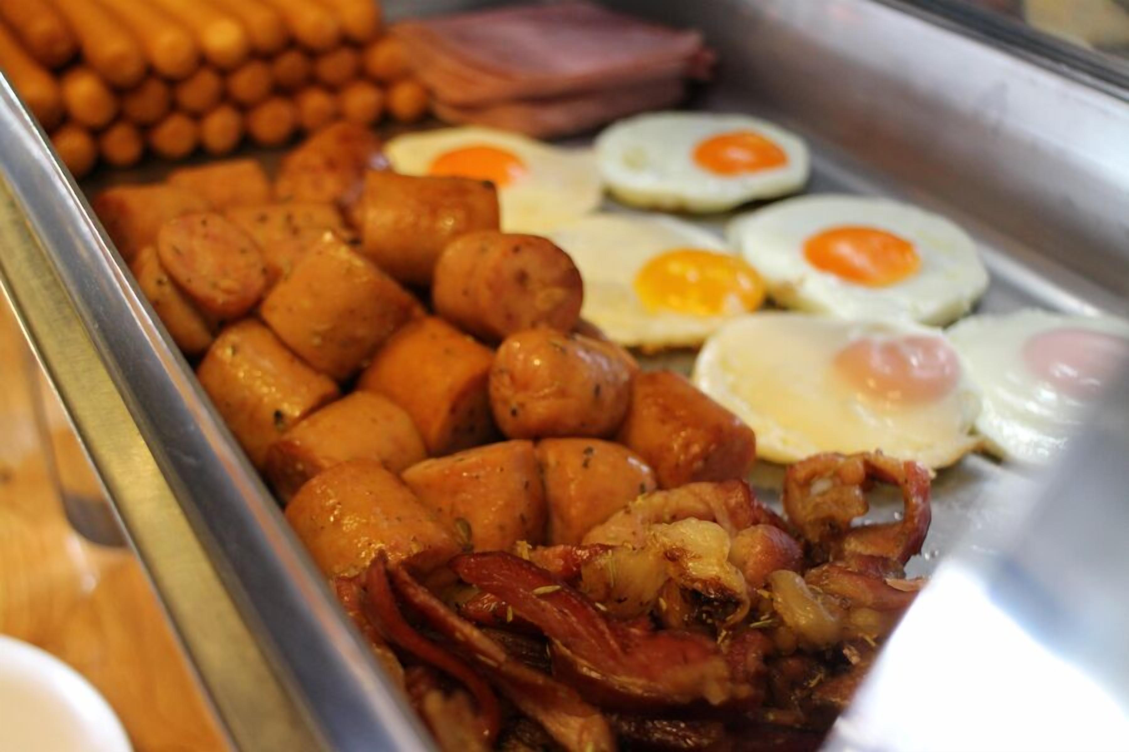 Un bufé con diversas opciones para el desayuno, incluyendo salchichas, huevos y tocino.