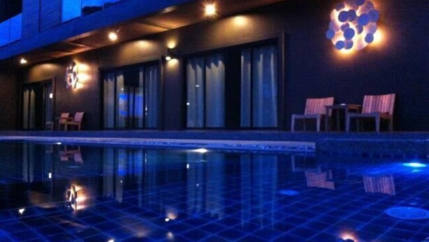 A modern hotel exterior with a swimming pool, outdoor seating, and a distinctive illuminated wall feature.