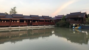 A row of traditional wooden buildings with tiled roofs, reflecting on calm water, and a small boat with a figure on it. - Win Resort Hat Yai (Hat Yai)