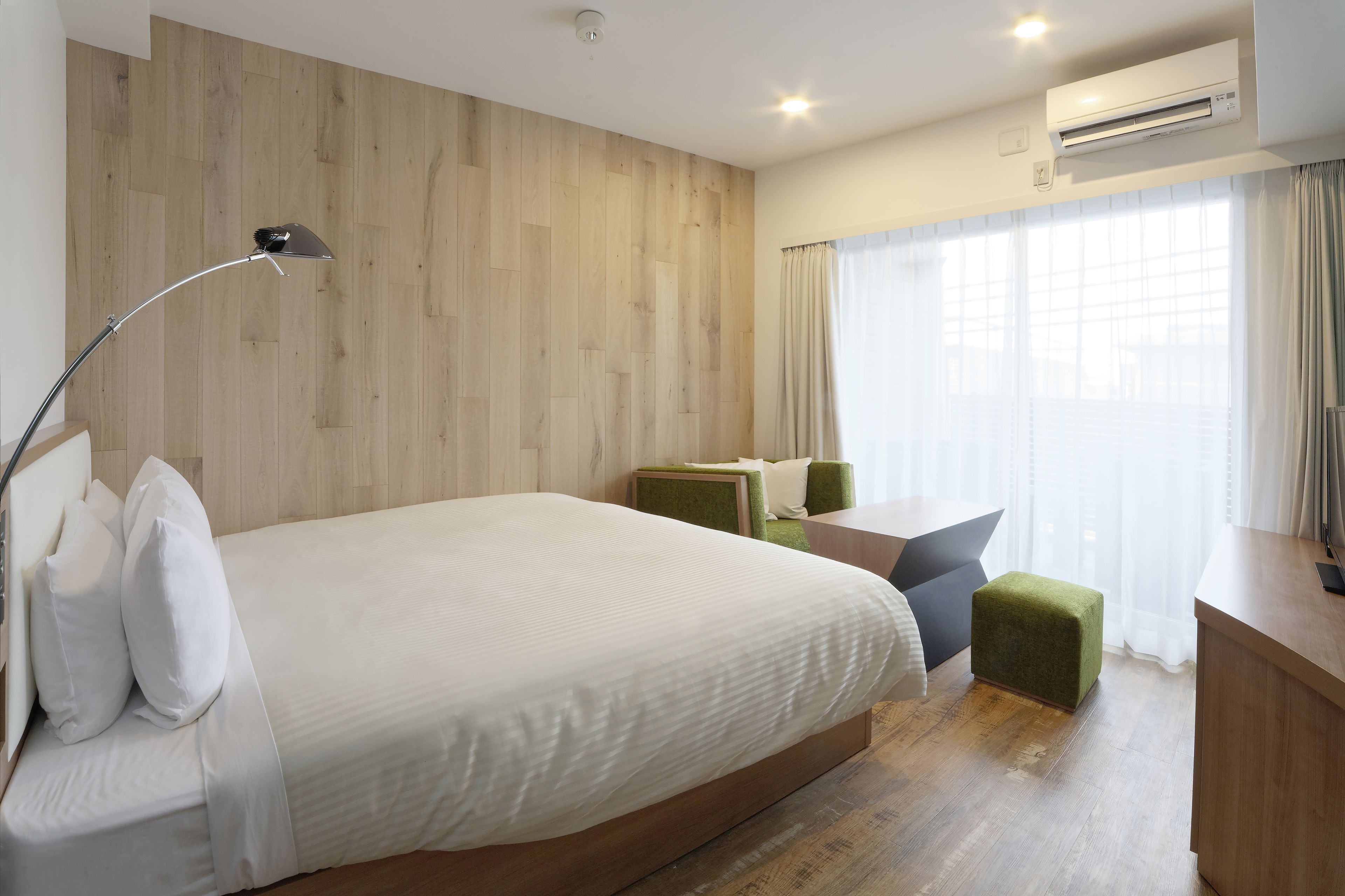 Hotellihuone, jossa on suuri sänky, työpöytä, tuoli ja pieni jalkarahi.