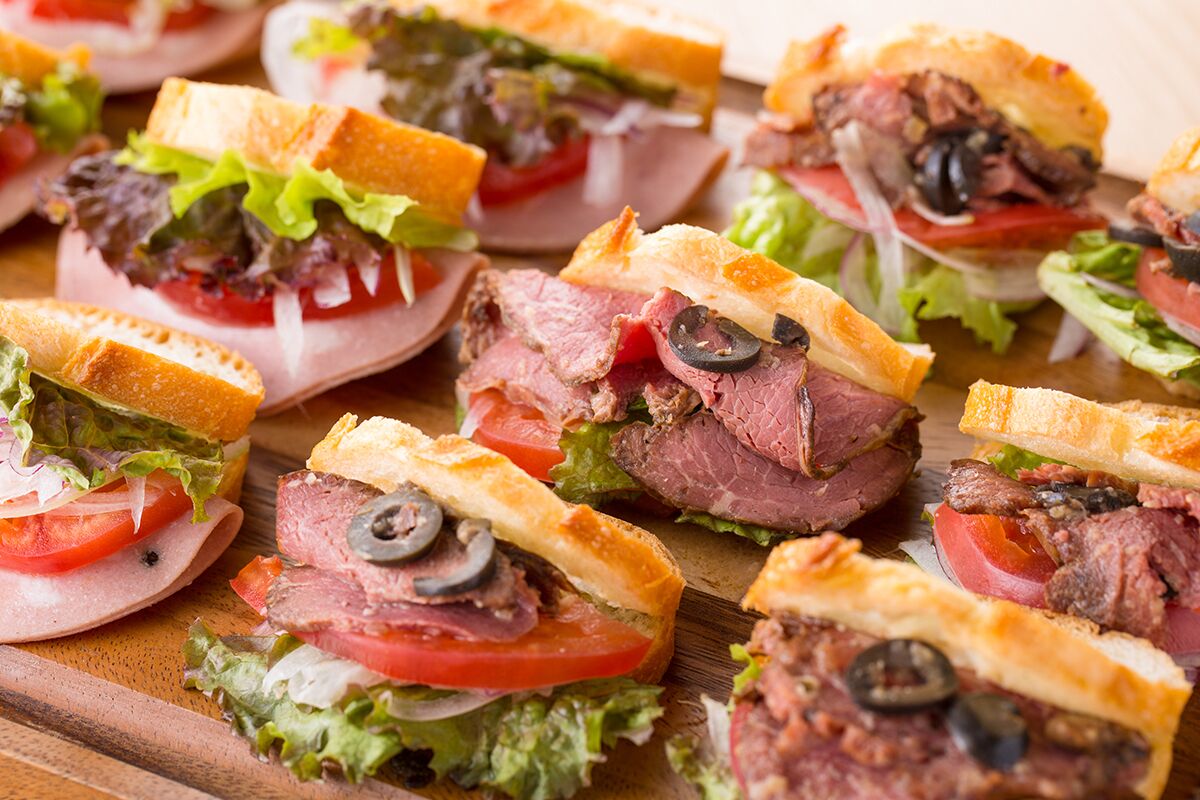A variety of sandwiches with different fillings, including meats, vegetables, and olives, arranged on a wooden board.