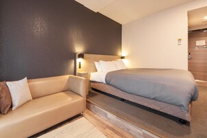 A modern hotel room with a bed, a sofa, and a nightstand with a lamp.