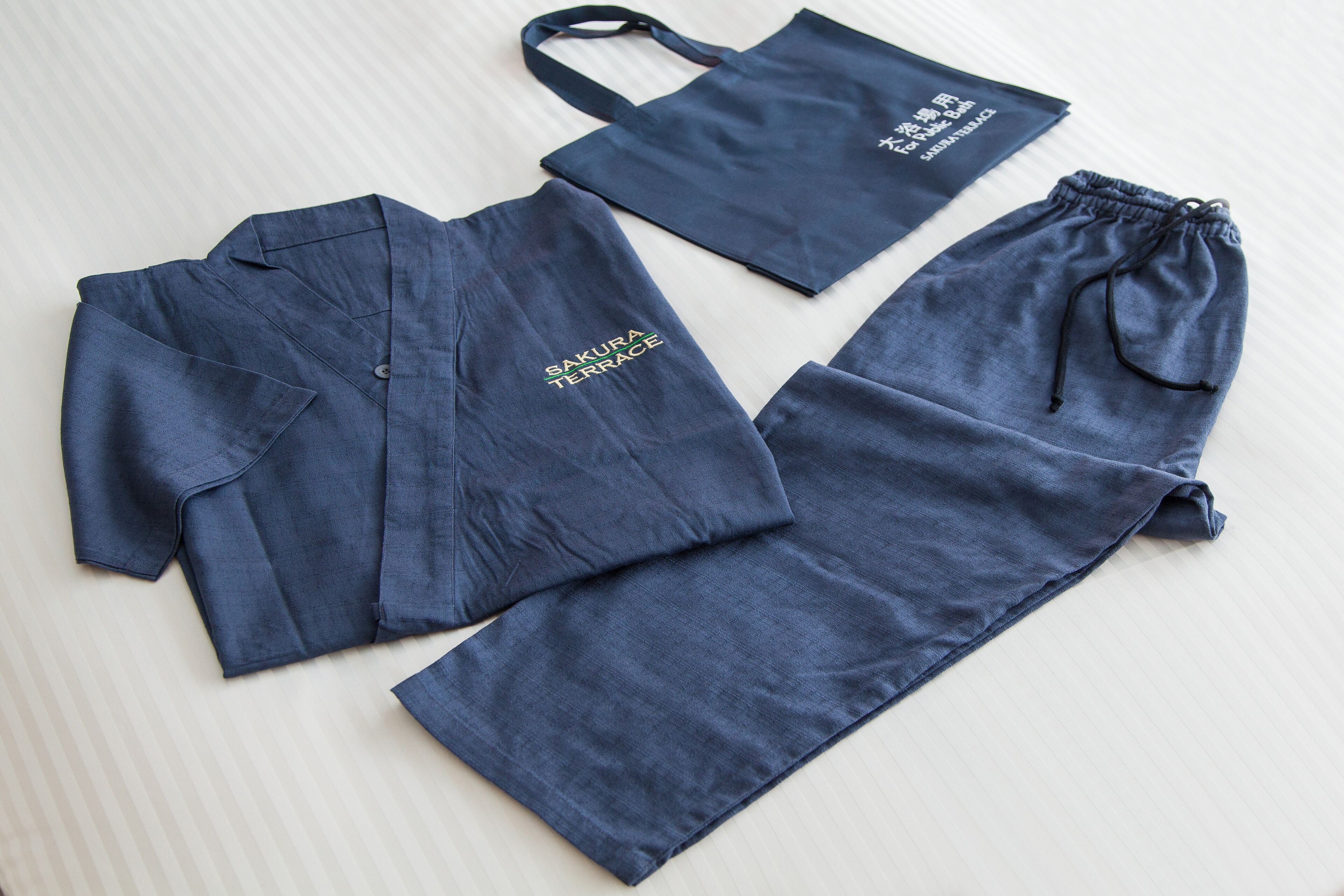 A set of blue clothing items including a shirt, pants, and a drawstring bag, all with the text "SAKURA TERRACE" on them.