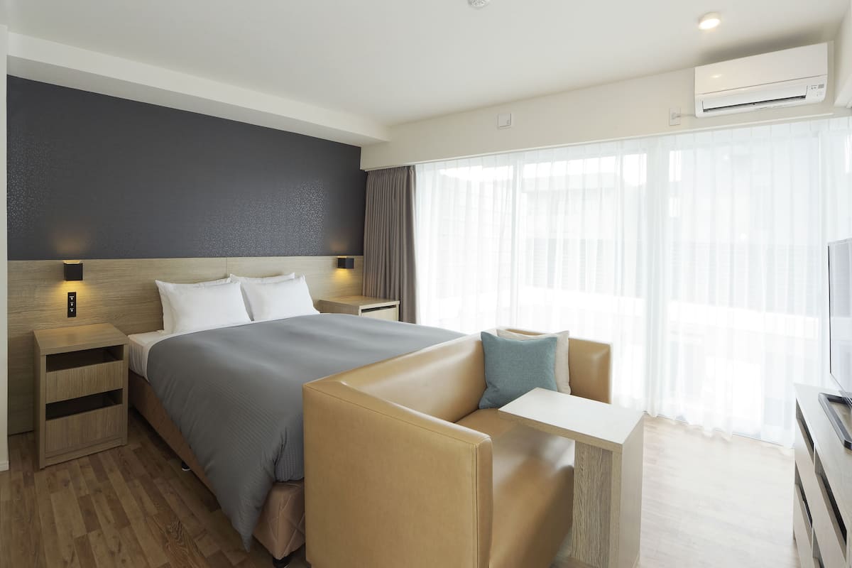 A modern hotel room with a large bed, a sofa, a small table, and a TV.
