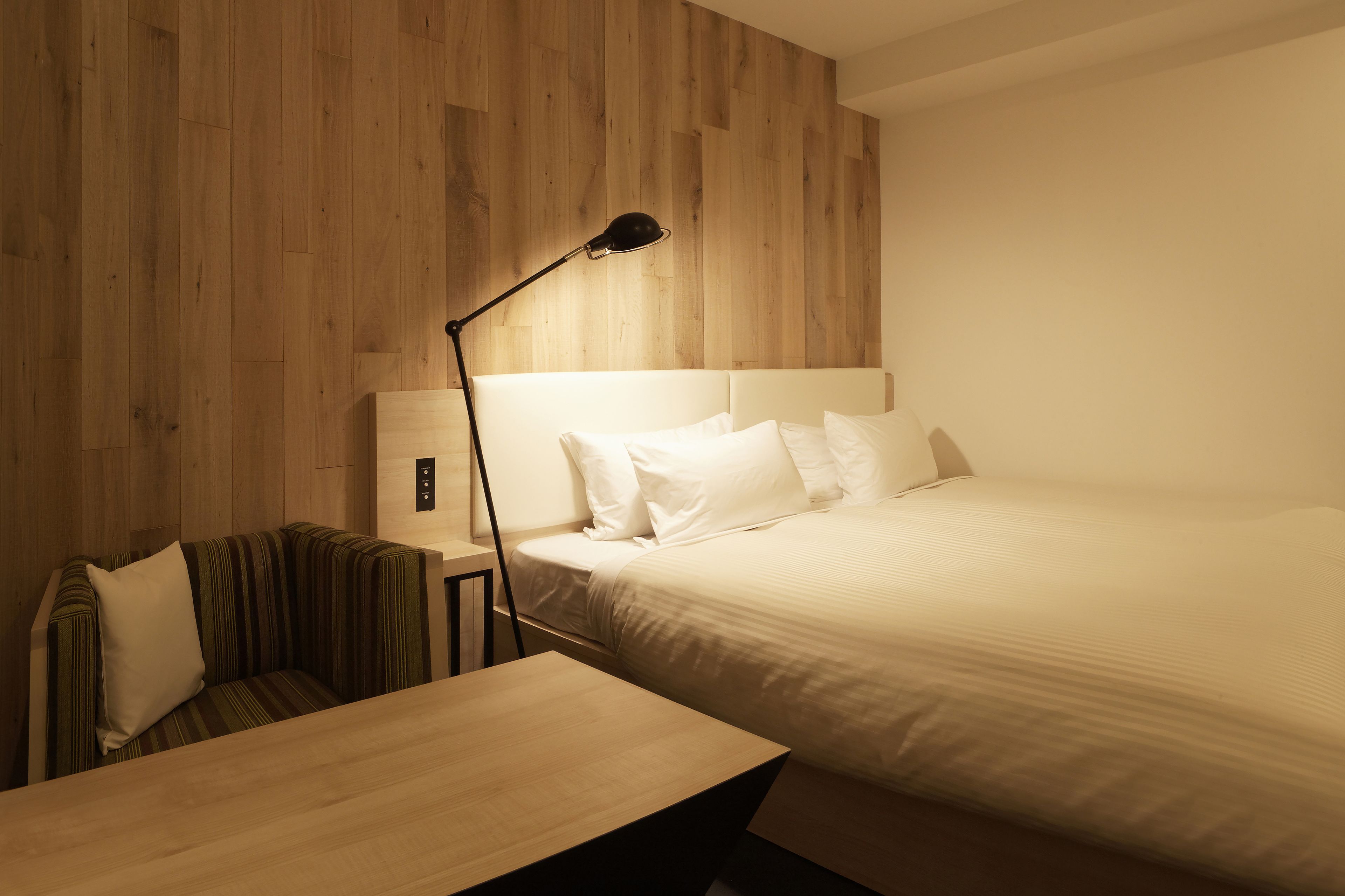 Un dormitorio con cabecera de madera, una mesita de noche, una lámpara y un banco a rayas.