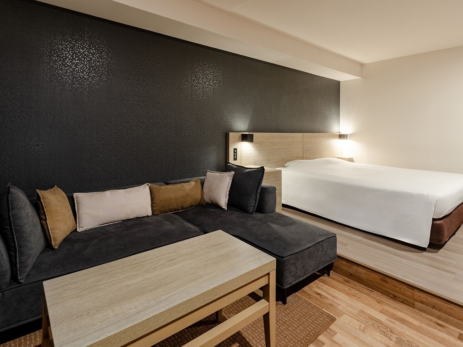 Une chambre d’hôtel moderne avec un canapé de couleur sombre, une table en bois et un lit simple.