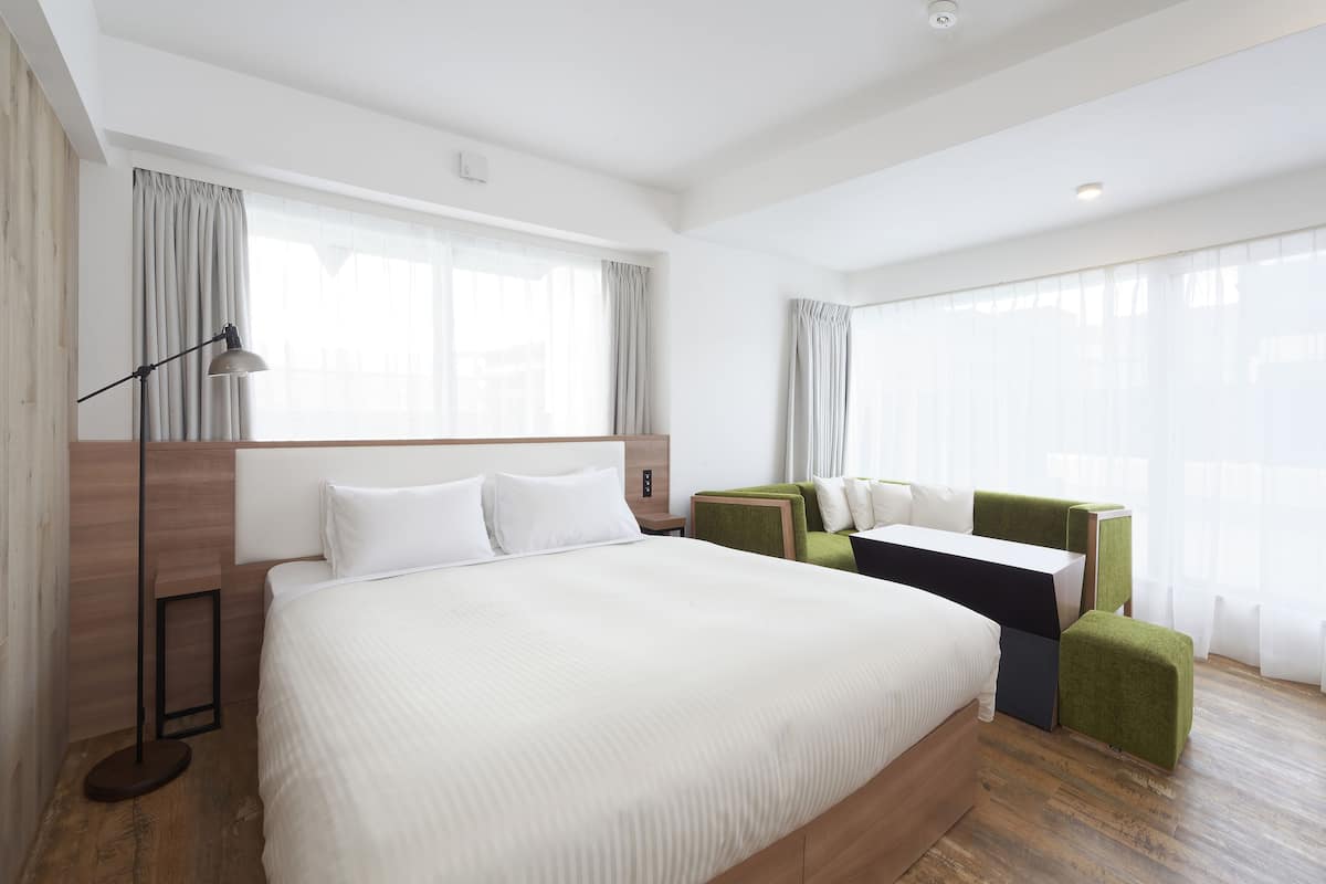 A modern hotel room with a large bed, a desk, and a green accent chair.