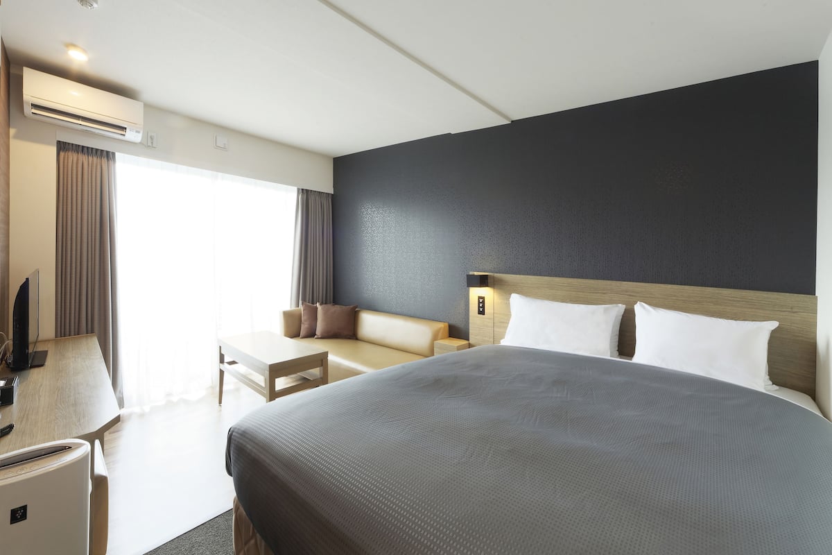 A hotel room with a large bed, a desk with a computer, a chair, and a sofa.