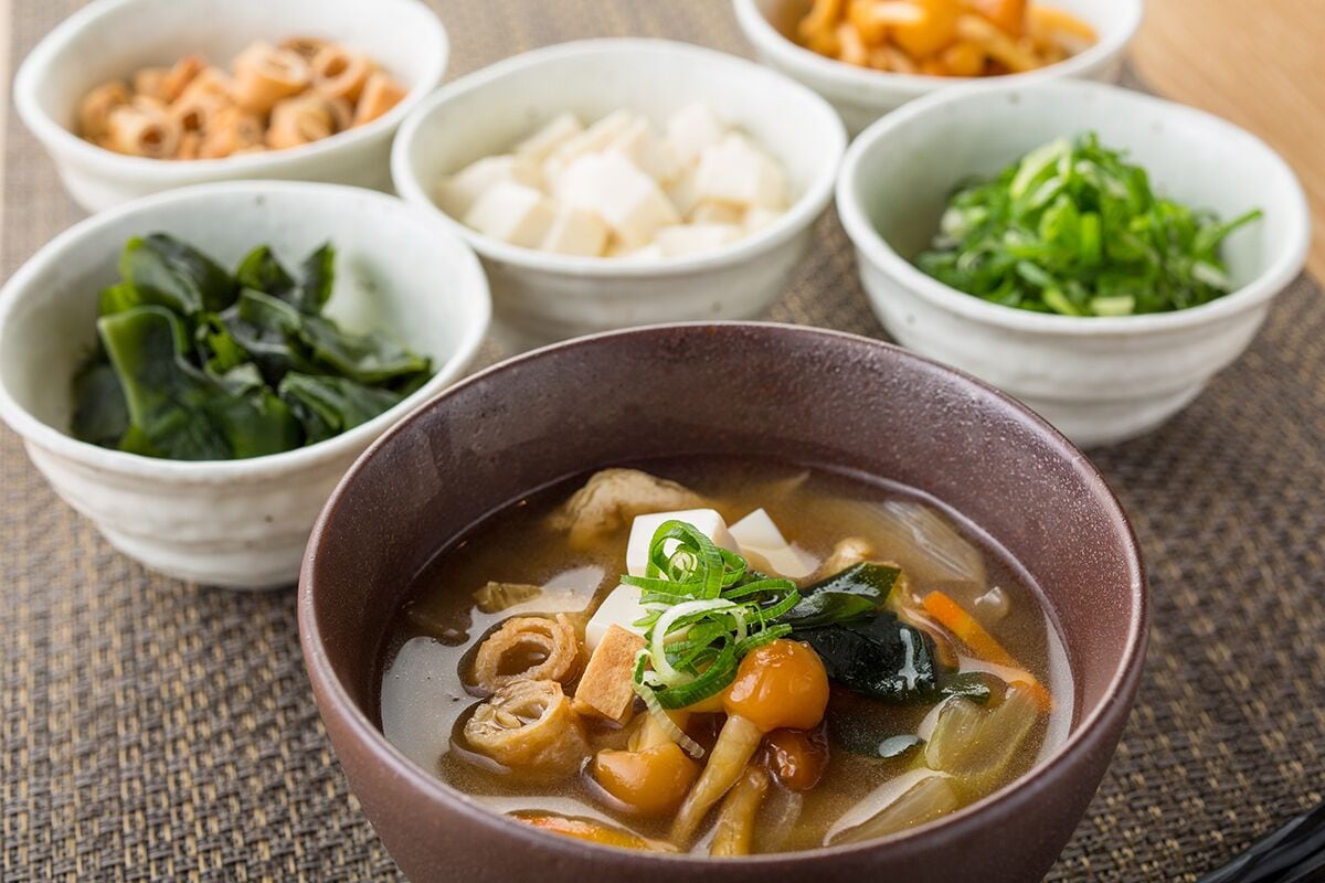 Un tazón de sopa acompañado de guarniciones variadas como tofu, alga marina y verduras.