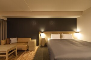 A modern hotel room with a large bed, a sofa, a wooden nightstand, and a desk.