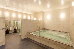 A modern bathroom with a large bathtub, marble walls, and a separate shower area.