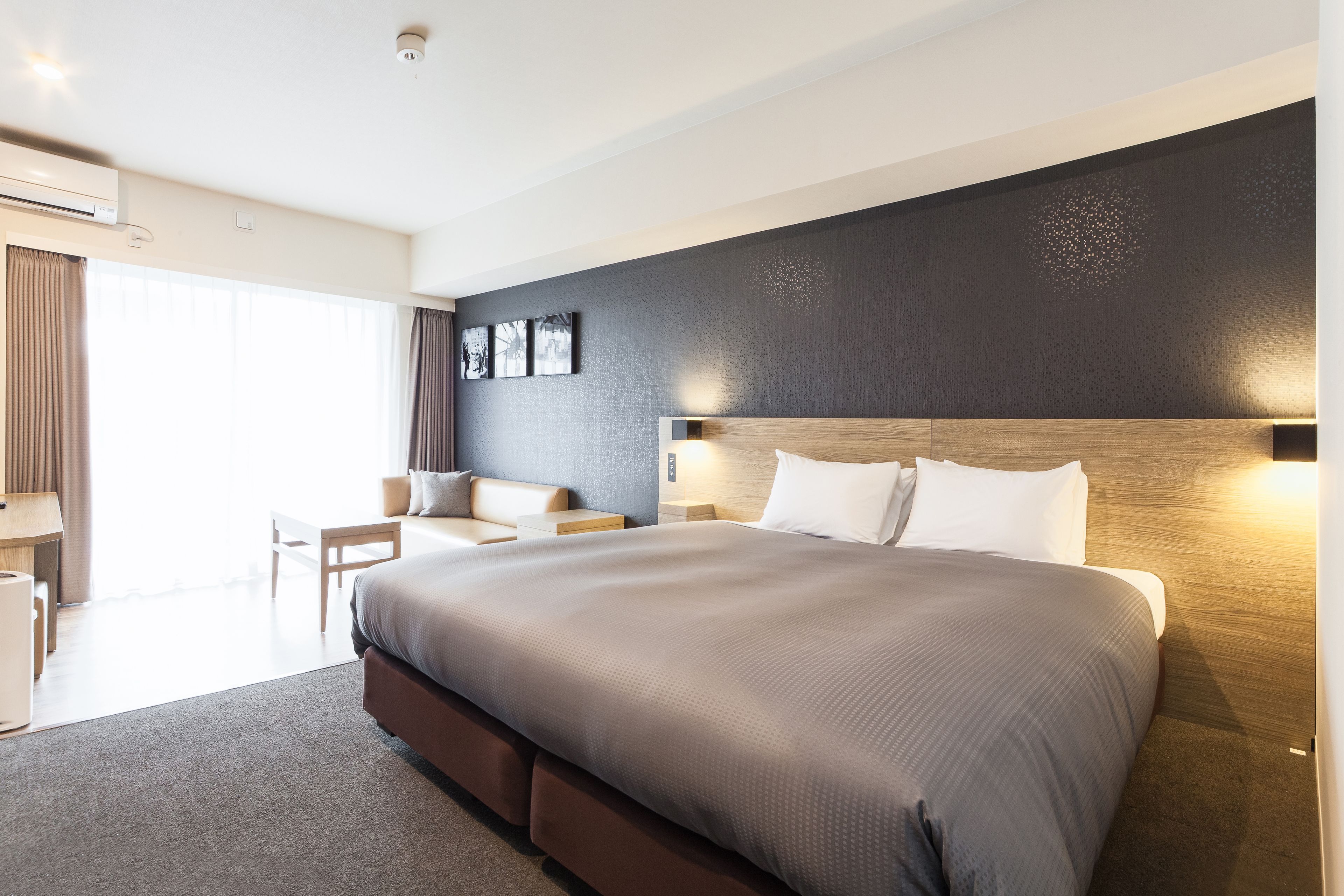 Una habitación de hotel moderna con una cama grande, un escritorio con silla, una mesita y un sofá.