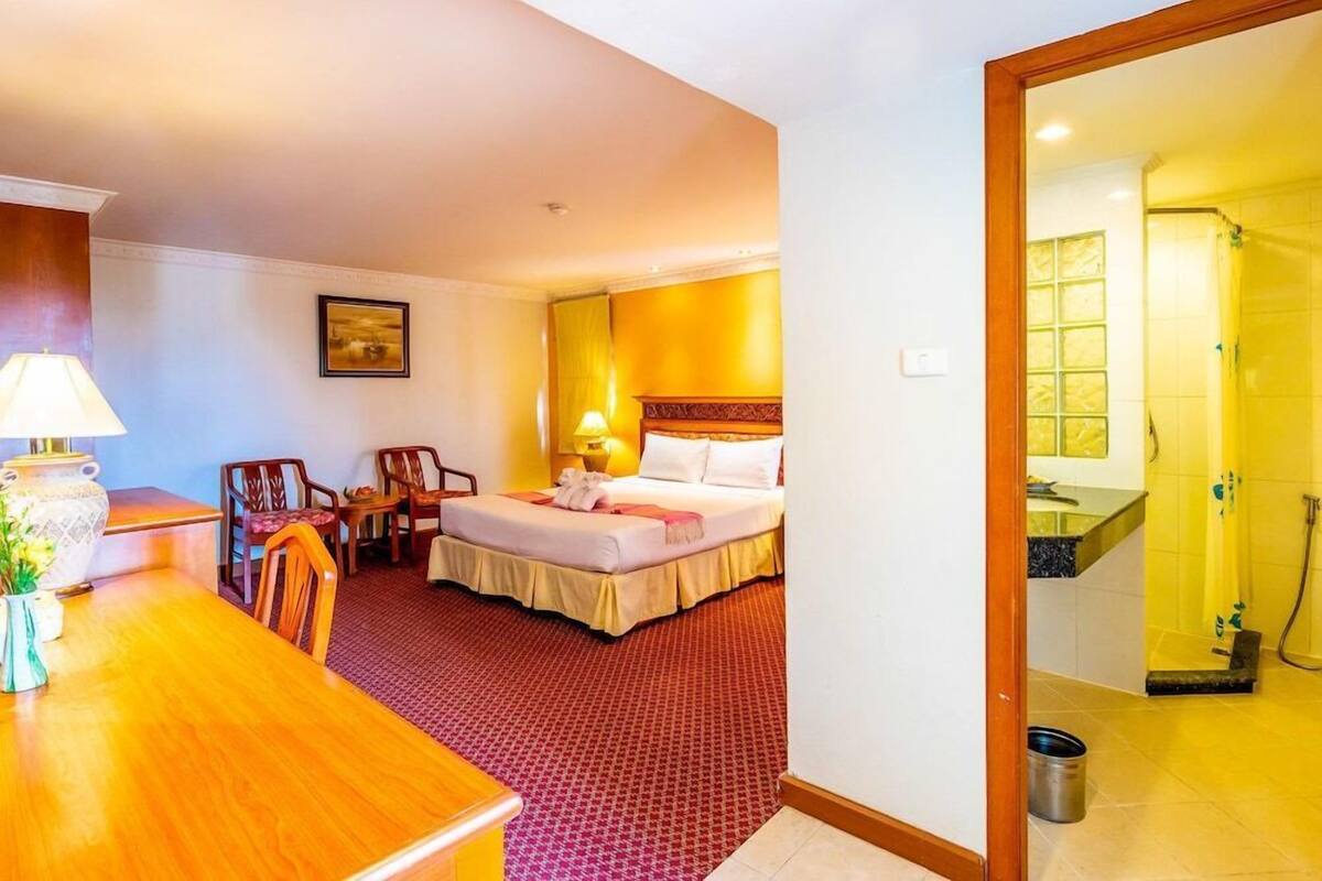 Une chambre d’hôtel avec un lit, un bureau, une chaise, une lampe et une salle de bain visible à travers une porte ouverte.