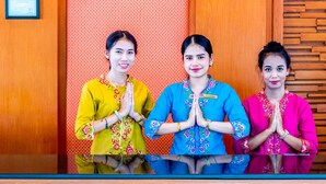 Three individuals standing in front of a reception desk with a patterned wall and wooden paneling. - Hatyai Paradise Hotel (Hat Yai)