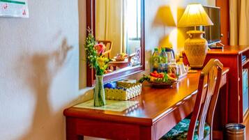 A hotel room with a wooden dining table, a chair, a lamp, a mirror, and a window with curtains.