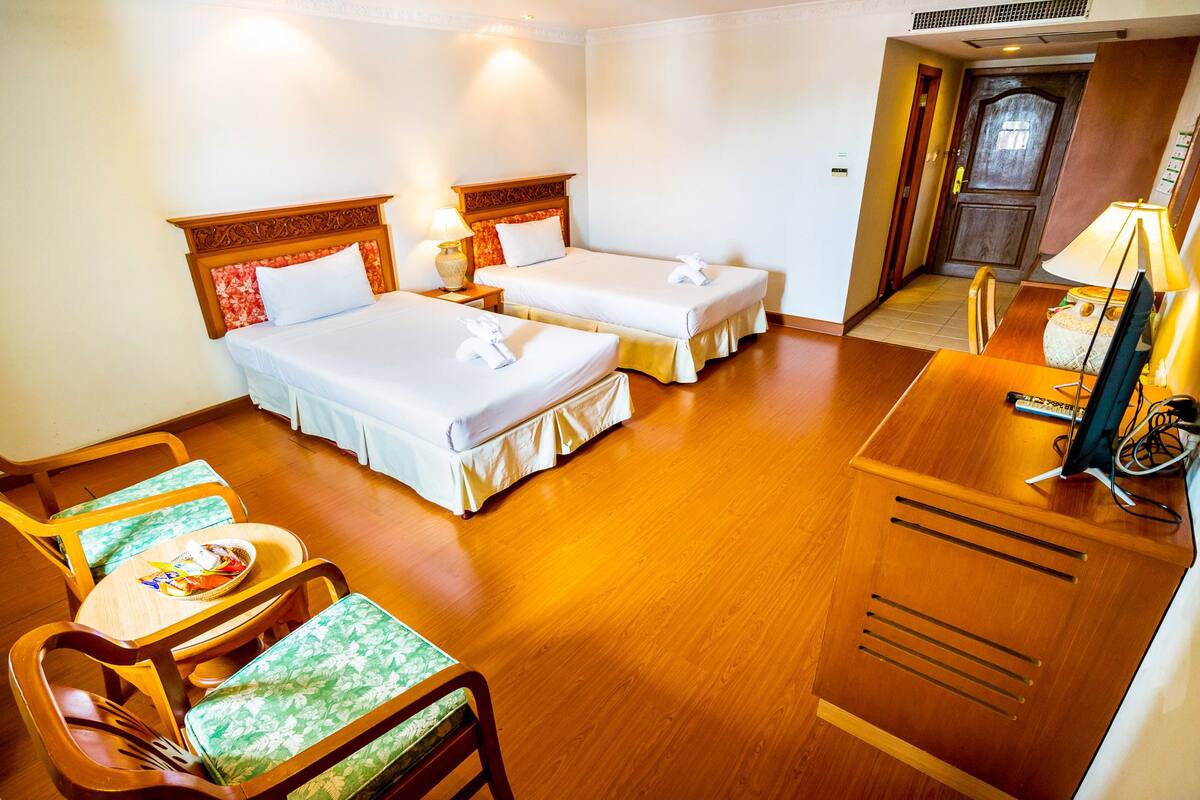 Une chambre d’hôtel avec deux lits, une petite table, des chaises, un bureau avec un ordinateur et une porte donnant sur une salle de bain.