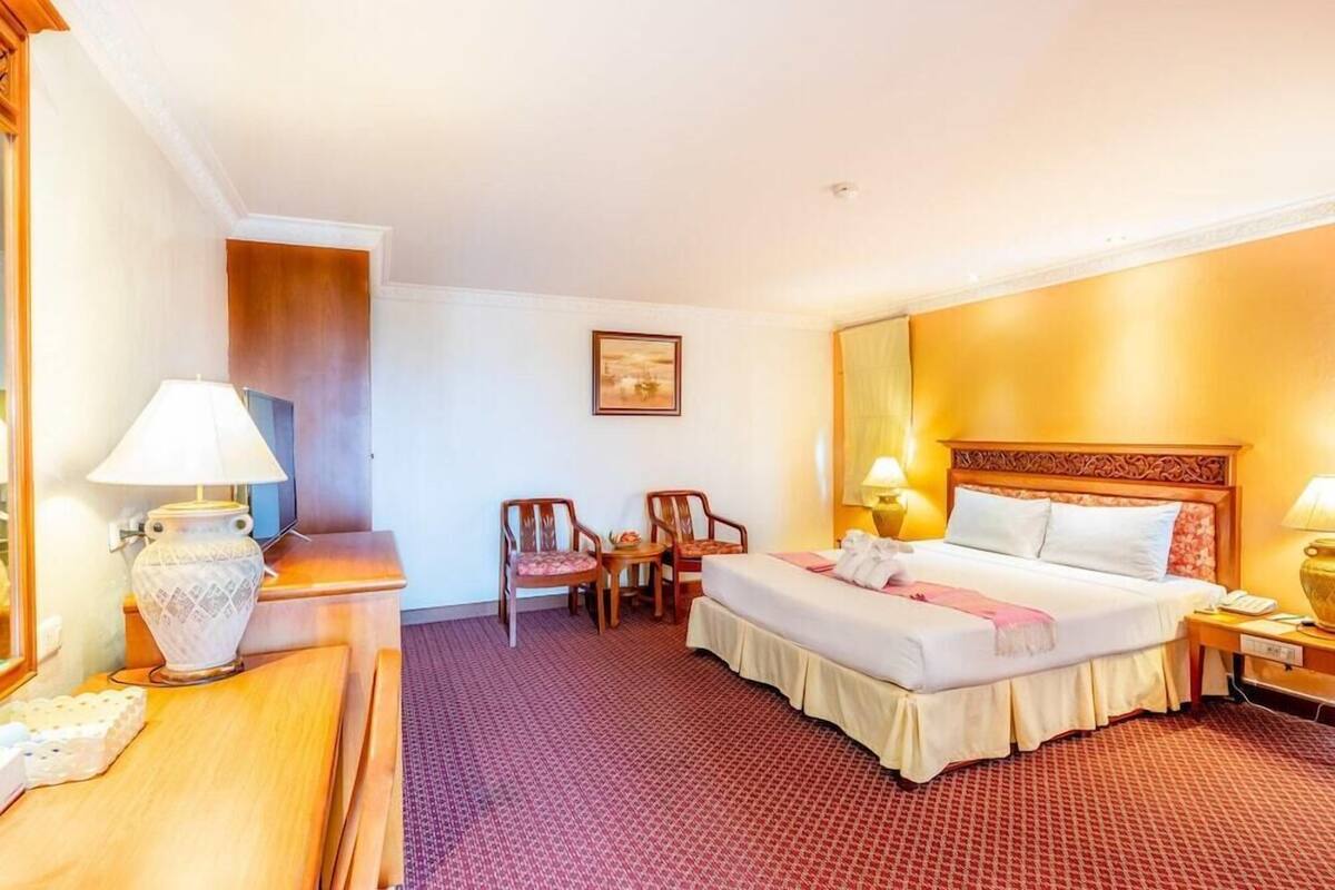 Une chambre d’hôtel avec un lit, deux chaises, un bureau, une lampe, un tableau au mur et un téléphone.
