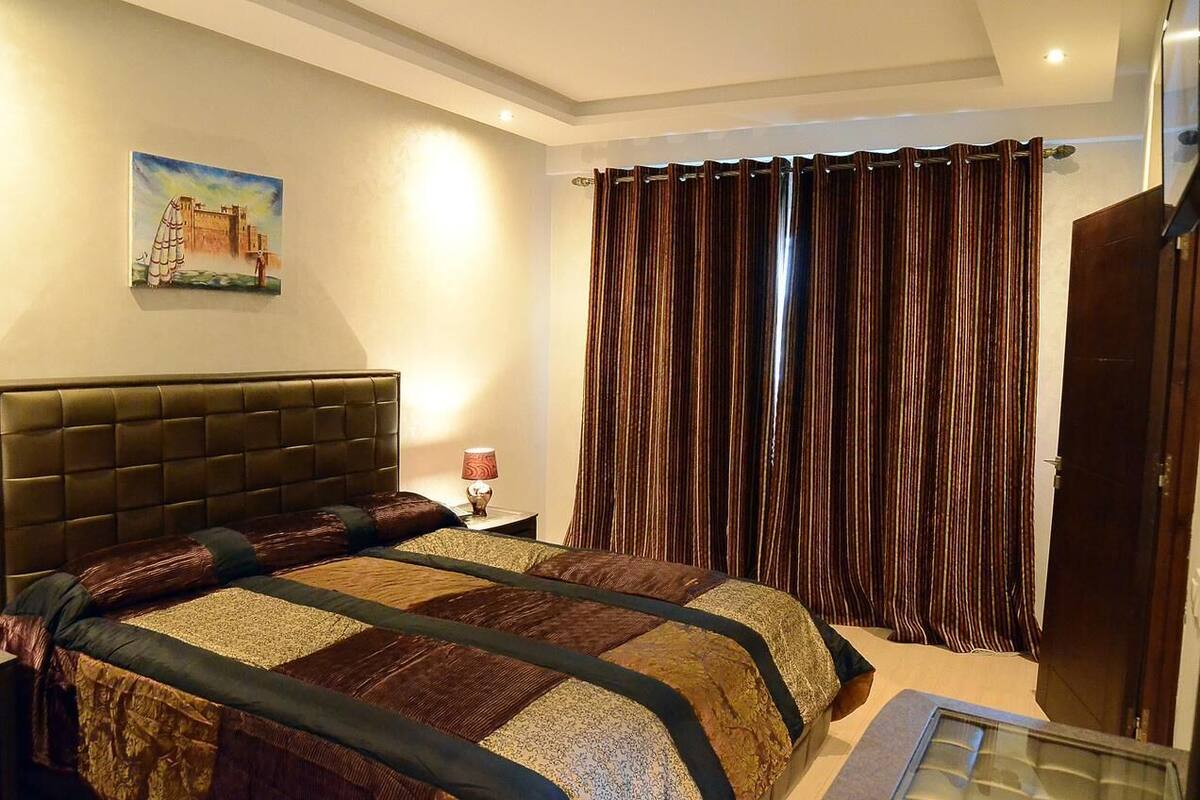 Ein Hotelzimmer mit einem großen Bett, einem Nachttisch mit Lampe, einem Bild an der Wand und einem Fenster mit Vorhängen.