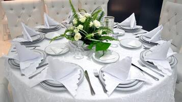 Una mesa redonda de comedor con mantel y servilletas blancas, y cubiertos dispuestos para una comida.