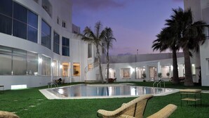 A modern hotel courtyard with a swimming pool, artificial grass, and wicker lounge chairs. - Hotel Chams (Tetouan)
