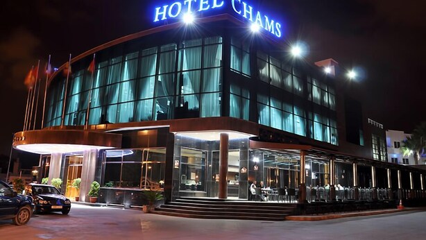 A modern hotel with a prominent "HOTEL CHAMS" sign, large glass windows, and a well-lit entrance area. - Hotel Chams (Tetouan)