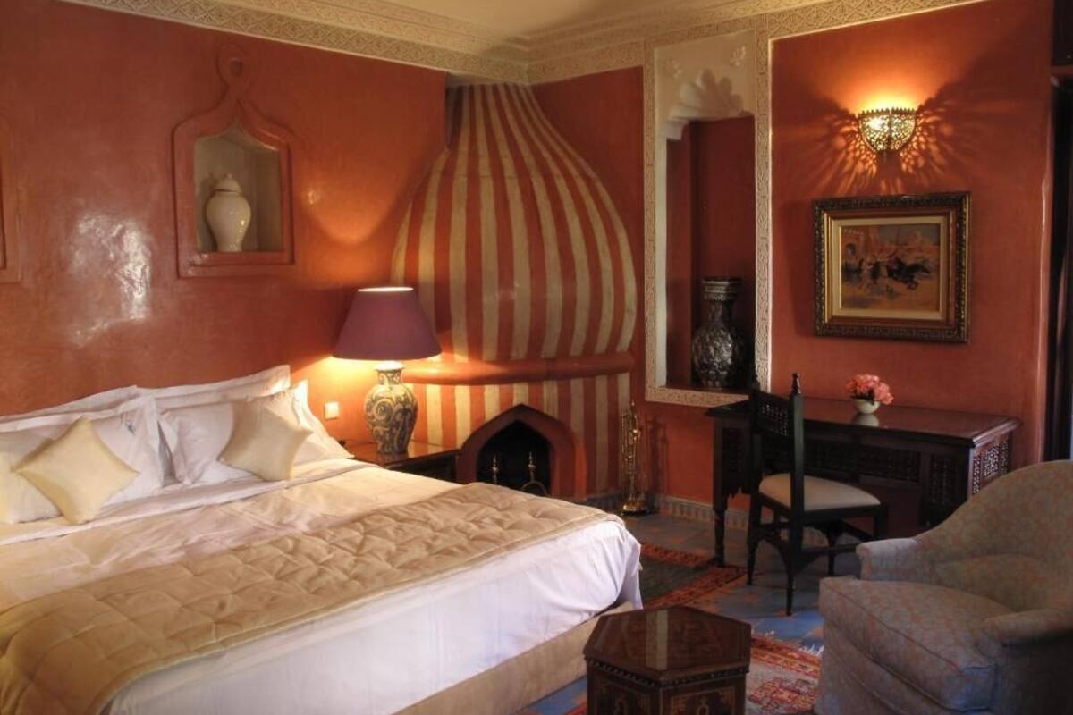 A hotel room with a large bed, a desk, a chair, and a decorative lamp.