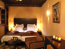 Una camera d'hotel con un letto grande, due comodini con lampade, un tavolino rotondo con un vaso di fiori e un quadro appeso al muro.