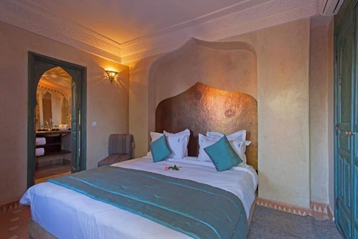 A hotel room with a large bed, a sitting area with a chair, a vanity with a mirror, and a door with a decorative handle.