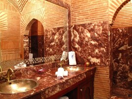 Une salle de bain avec un lavabo en marbre, un grand miroir et un mur recouvert de carreaux.