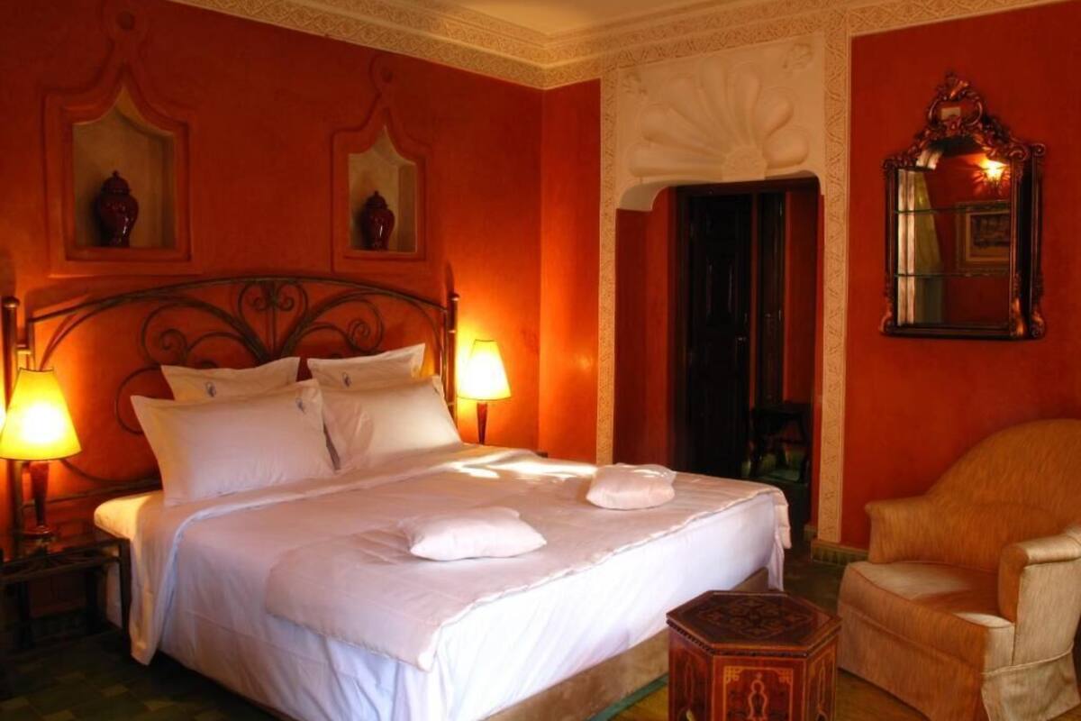 A hotel room with a large bed, two bedside lamps, a chair, and a small table.