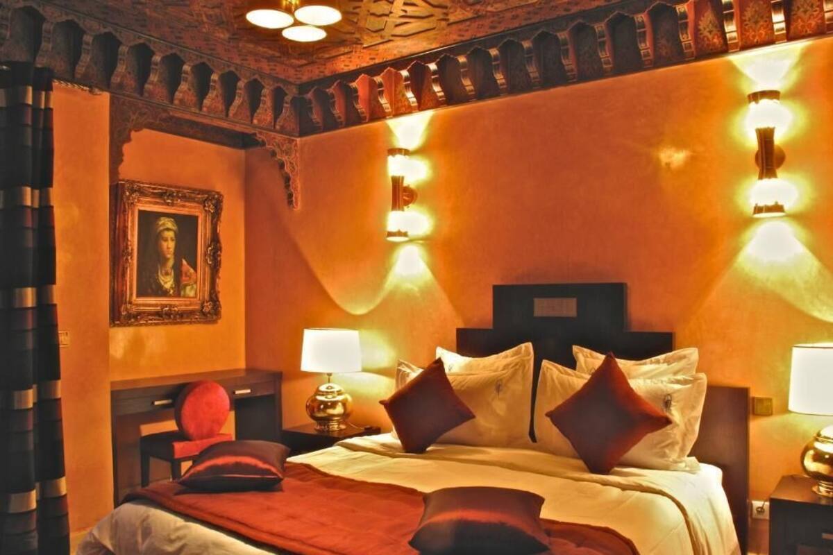 A hotel room with a large bed, ornate ceiling, and wall-mounted lighting.