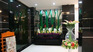 Um lobby moderno com um sofá preto, uma cadeira de madeira e um arranjo floral grande.