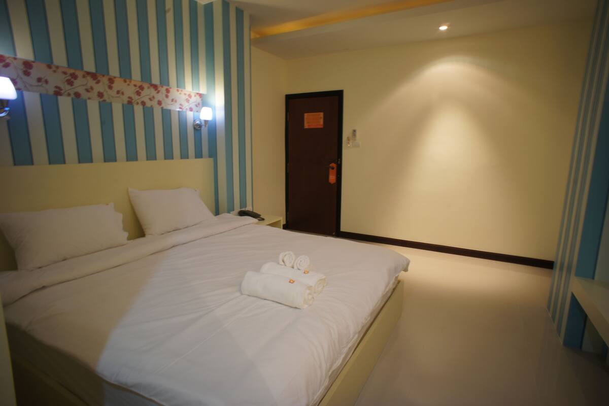 Une chambre d’hôtel avec un grand lit, un papier peint à rayures et une porte avec une pancarte.