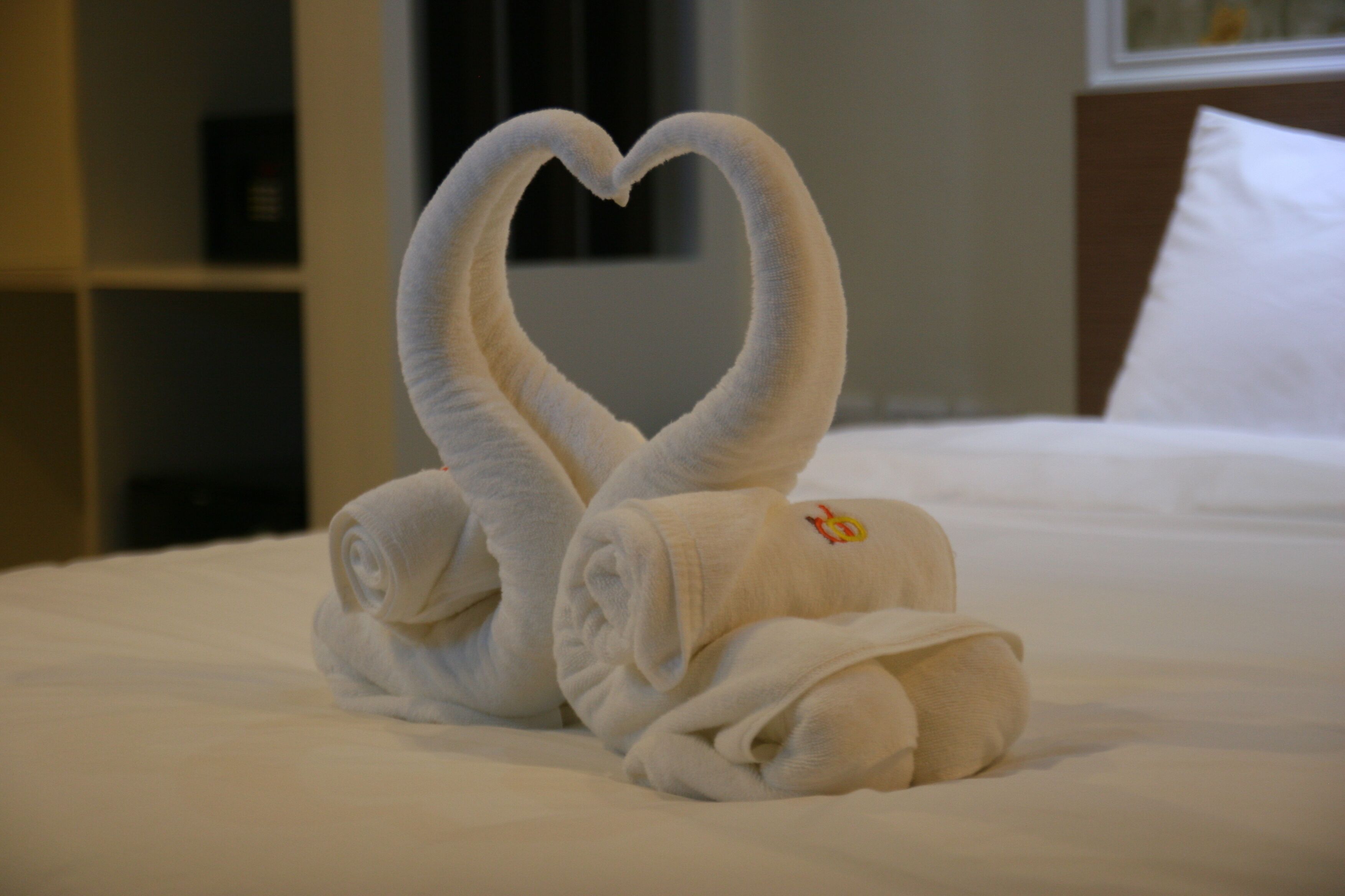 A bed with two towels folded into a heart shape.