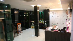 Uma área de recepção moderna com um balcão escuro, entrada de vidro e um arranjo floral decorativo.