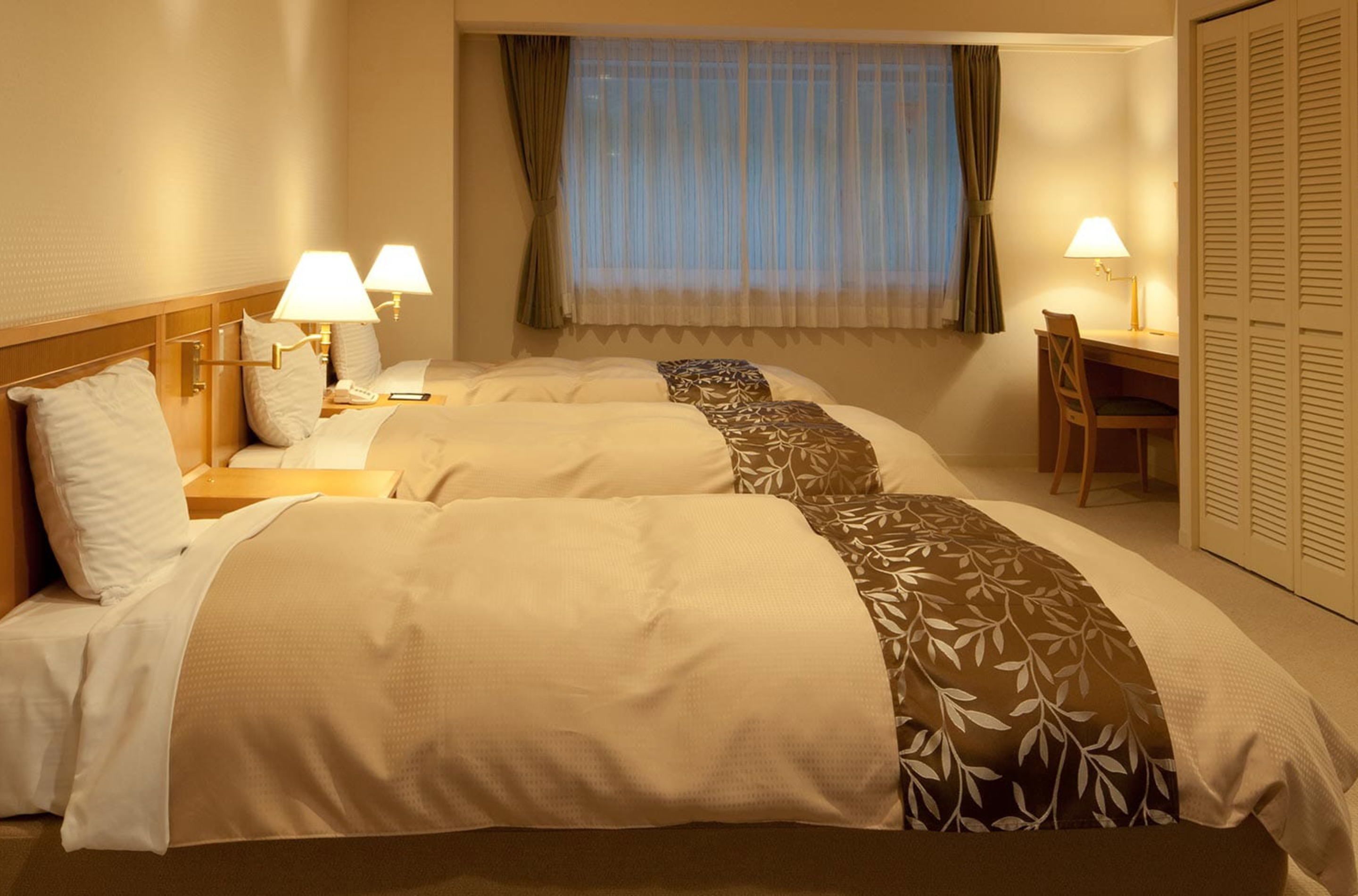 A hotel room with two beds, bedside lamps, a desk, and a chair.