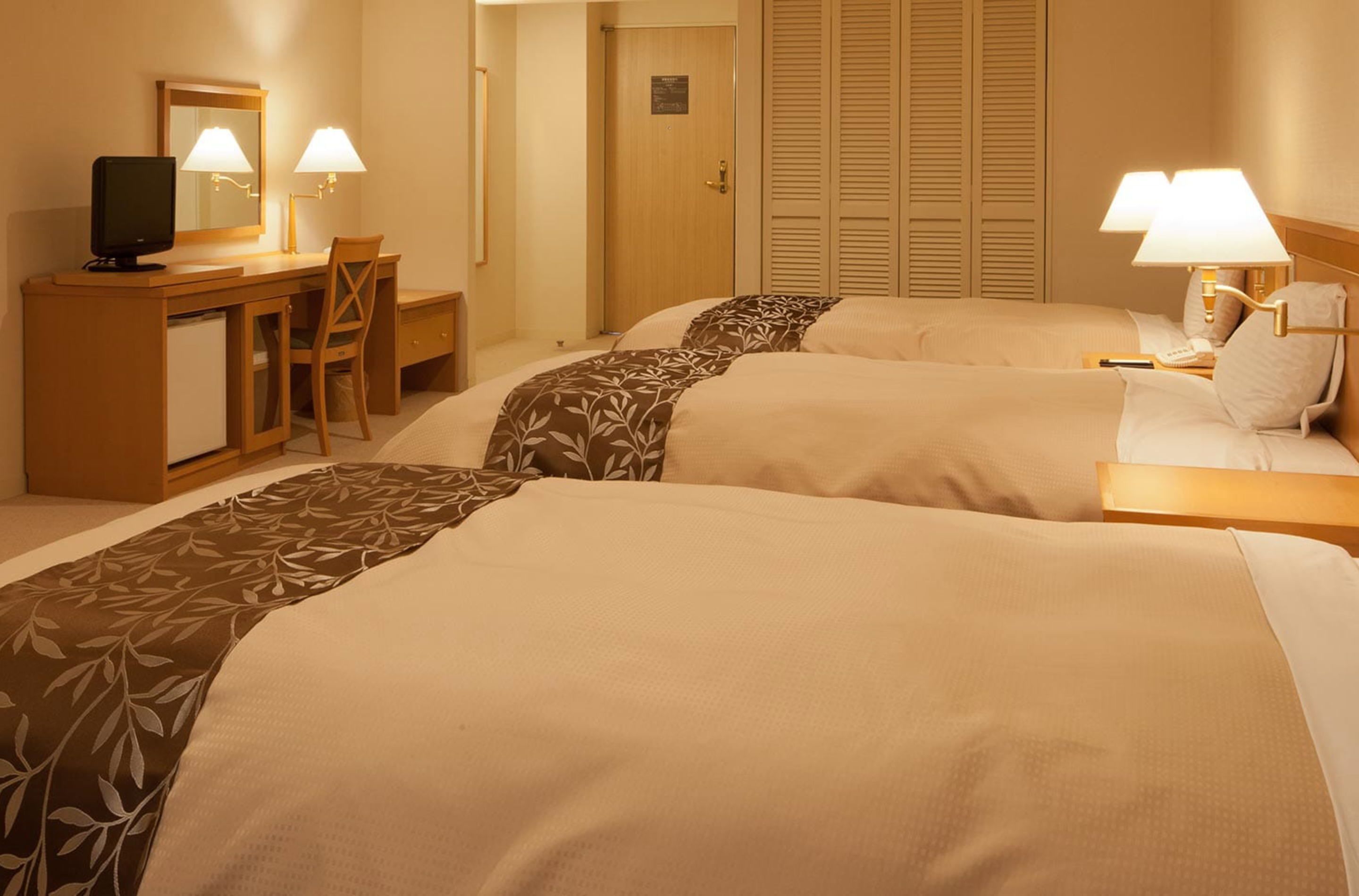 A hotel room with two beds, a desk with a computer and lamp, and a wardrobe.