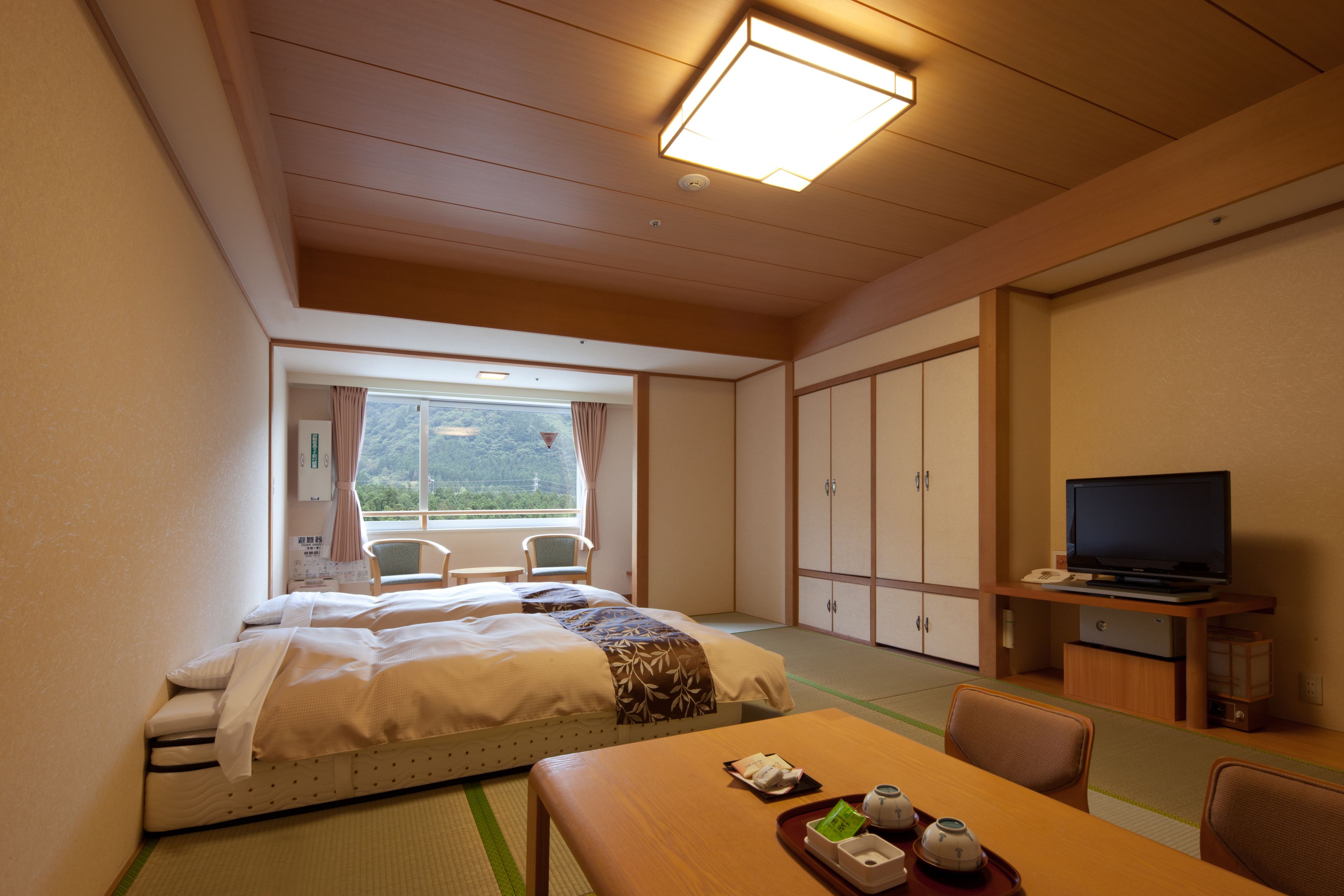 A hotel room with a bed, a dining table, chairs, a television, and a view of the outdoors.
