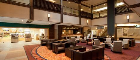 A spacious lobby with multiple seating areas, a central coffee station, and a visible staircase leading to an upper level.