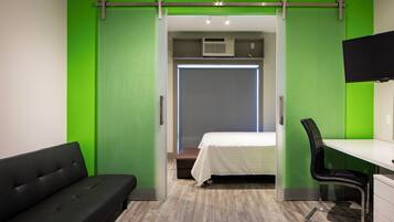 Una habitación de hotel moderna con una pared de acento verde, una cama, un escritorio con una silla y un sofá.