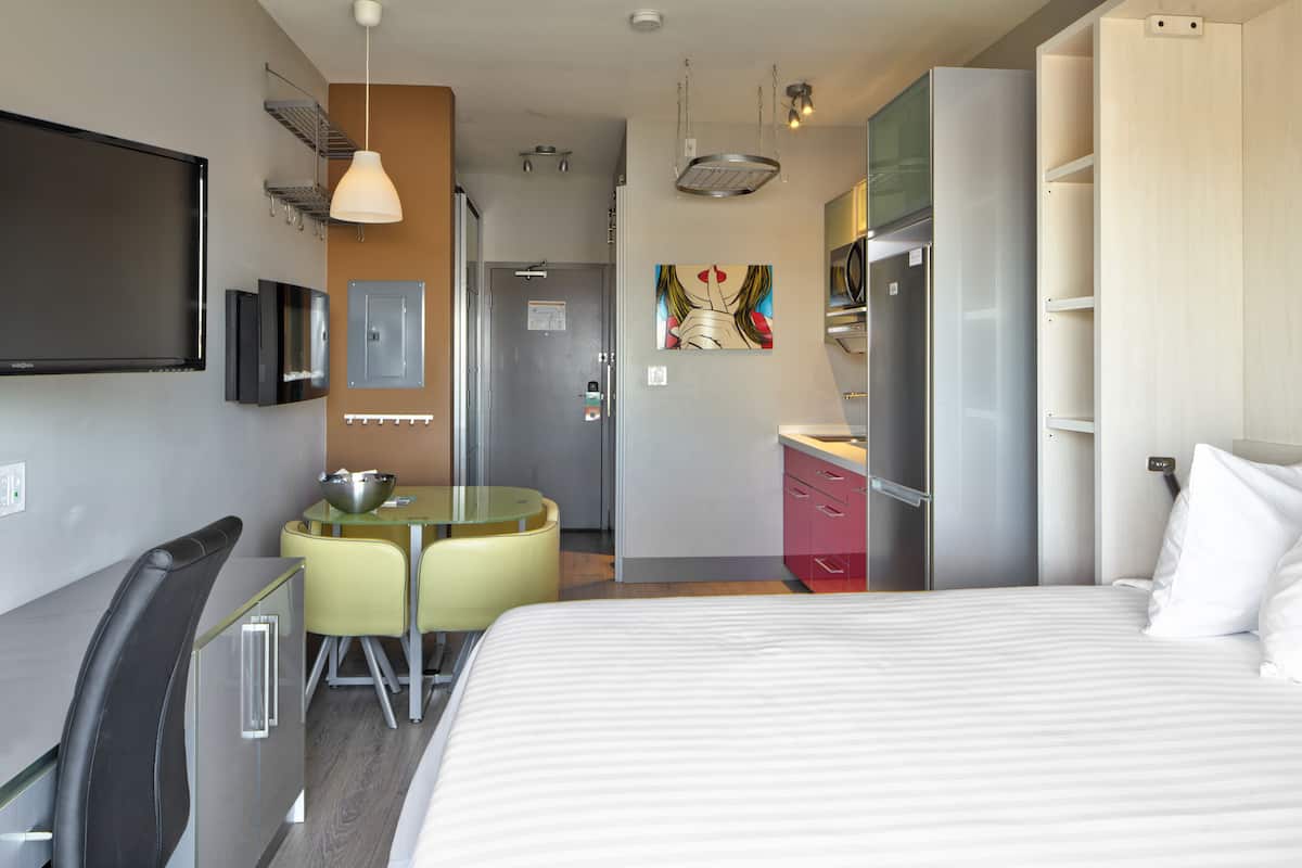 A hotel room with a bed, a desk, a chair, a TV, a microwave, and a refrigerator.