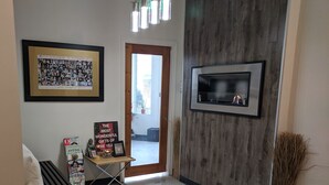 Zona de recepción con un cuadro enmarcado, una mesa pequeña con revistas, chimenea y un muro decorativo de madera.