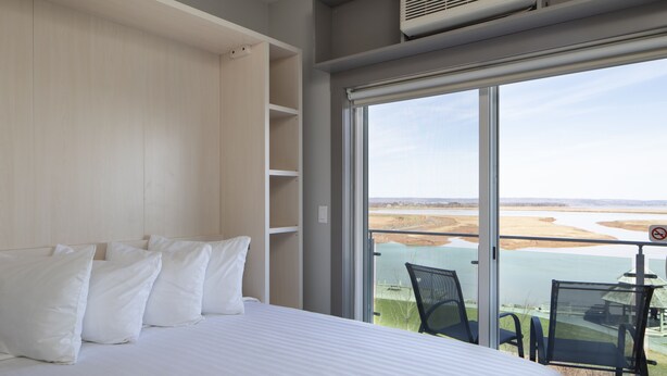 Un dormitorio con una cama grande, almohadas blancas y vista a un cuerpo de agua a través de una puerta corrediza de vidrio.