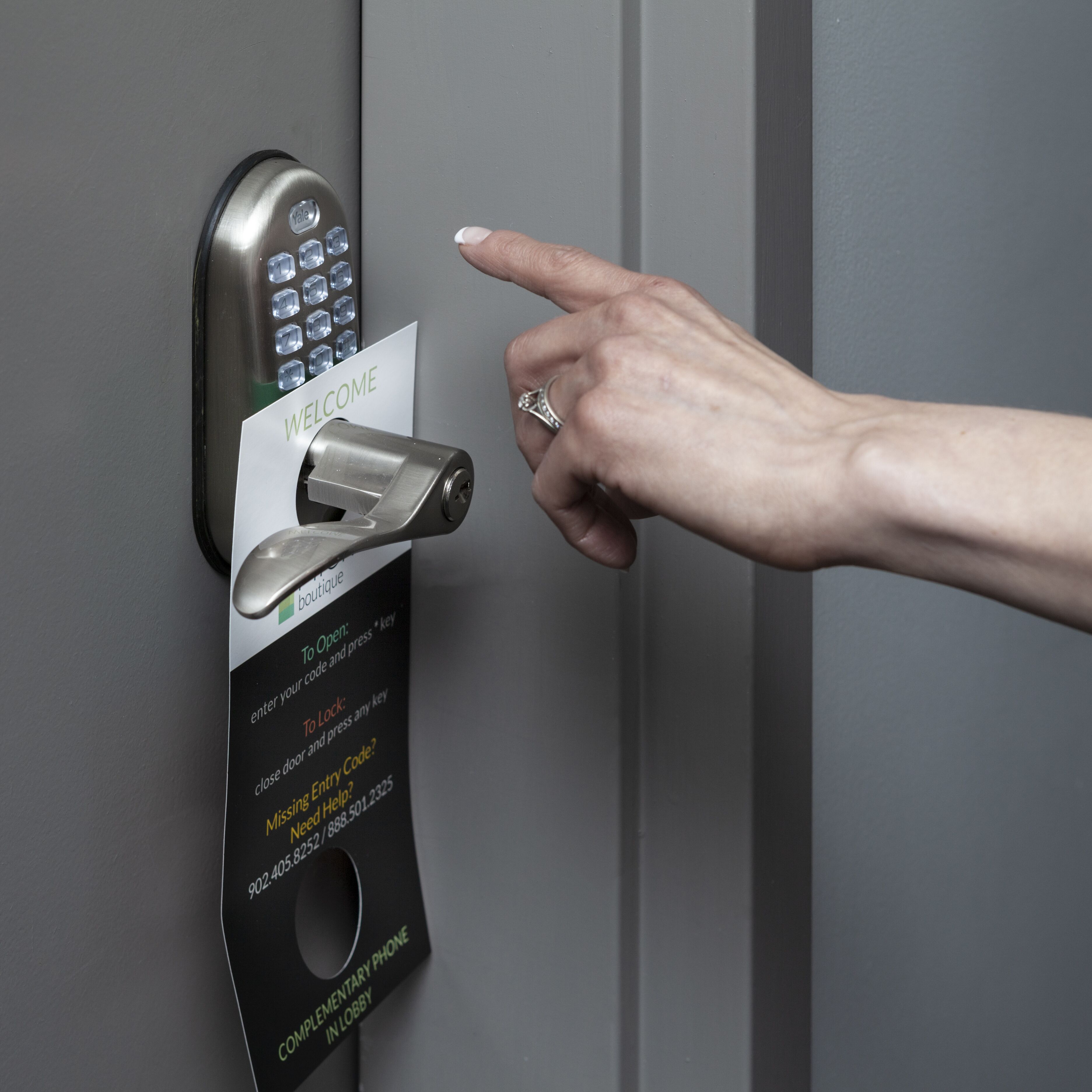 Een hand gebruikt een sleutelkortje om een deur met een keypad te openen, met een 'WELCOME' bordje.